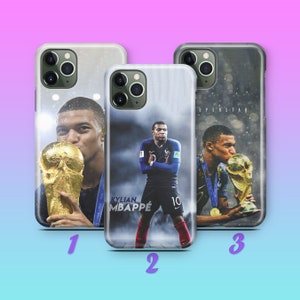 Puede incluir: Tres fundas de teléfono diferentes con un jugador de fútbol sosteniendo un trofeo. La primera funda presenta un primer plano del jugador sosteniendo el trofeo. La segunda funda presenta al jugador de pie con el trofeo en el fondo. La tercera funda presenta al jugador besando el trofeo. Las tres fundas tienen un fondo blanco con una imagen borrosa de un estadio en el fondo.
