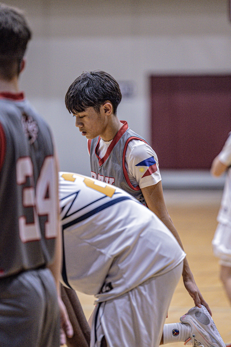 May include: Three basketball players in a game, one player is wearing a grey jersey with a red and white stripe and a Philippine flag patch on the right shoulder, another player is wearing a white jersey with a blue and yellow stripe, and the third player is wearing a grey jersey with a red and white stripe and the number 34 on the front.