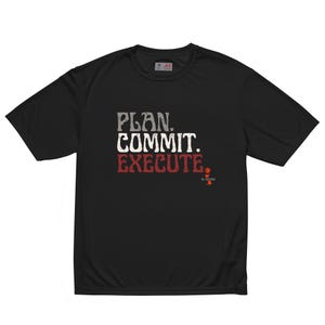 May include: Black t-shirt with the words "PLAN. COMMIT. EXECUTE." in a distressed font. The text is in gray, white, and red. The shirt has a crew neck and short sleeves. The brand logo is visible on the upper back.