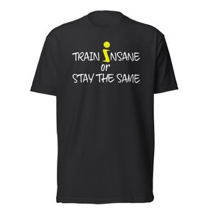 May include: A black short-sleeved t-shirt featuring the white text "TRAIN INSANE OR STAY THE SAME" printed on the chest. The letter "I" in "INSANE" is replaced by a yellow tennis ball graphic. The shirt has a crew neckline and a standard fit.