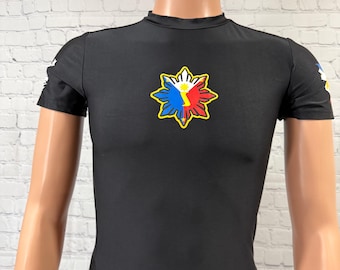 May include: Black short-sleeve shirt featuring a colorful emblem on the chest. The emblem is a sunburst design with red, white, blue, and yellow accents. The shirt is displayed on a mannequin.