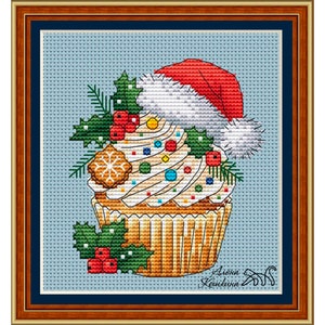 May include: A white cupcake with colorful sprinkles and a red and white Santa hat. The cupcake is decorated with holly and a gingerbread cookie. The text "Алёна Кошкииа" is written in the bottom right corner.