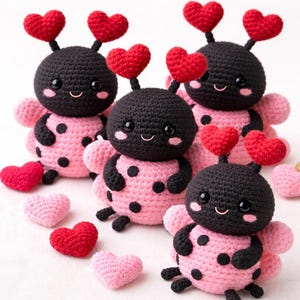 May include: Crocheted ladybug dolls with pink polka-dotted bodies, black heads, and red heart antennae. The dolls have smiling faces and pink wings. Several crocheted red and pink hearts are scattered around the dolls.