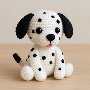 Puede incluir: Un juguete de perro dálmata tejido a ganchillo, blanco con manchas negras, orejas y ojos negros. El juguete tiene una lengua rosa y está sentado sobre una superficie de madera.