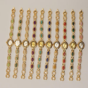 Puede incluir: Una colecci&oacute;n de relojes de pulsera dorados con esferas ovaladas y correas a juego. Cada correa presenta una serie de piedras preciosas ovaladas de colores, incluyendo verde, morado, azul y rojo. Las esferas de los relojes son doradas o plateadas.