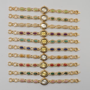Puede incluir: Una colecci&oacute;n de relojes de pulsera dorados con esferas ovaladas y correas adornadas con piedras preciosas de colores. Las esferas del reloj muestran la hora. Las piedras preciosas son de varios colores, incluyendo verde, azul, rojo y rosa.