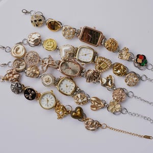 Puede incluir: Una colección de relojes de mujer de estilo vintage con correas decorativas. Las correas presentan varios adornos, incluyendo botones, corazones, flores y perlas. Las esferas de los relojes tienen varias formas, incluyendo cuadradas y redondas, con tonos dorados y plateados.
