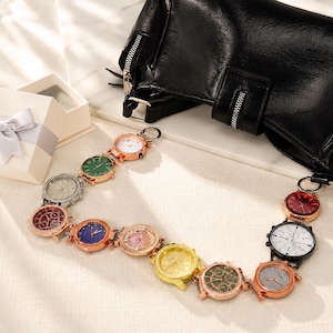 May include: A collection of colorful, round watches with various face designs, linked together. The watches have rose gold-colored bezels and are arranged in a chain. A black leather bag and a gift box with a silver ribbon are in the background.