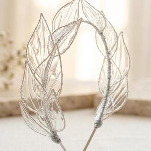 May include: A silver-toned headband featuring a series of translucent, clear leaf-shaped elements. Each leaf is outlined with a metallic silver wire, and the leaves are attached to a thin, flexible silver-coloured metal band with wire wrapping.