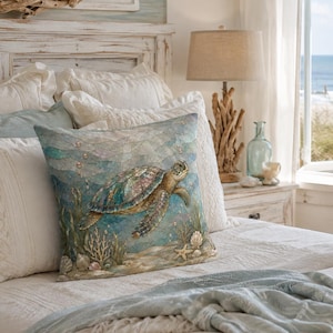 May include: A square throw pillow featuring a detailed illustration of a sea turtle swimming through blue ocean water with coral, seashells, and a starfish at the bottom. The pillow is placed on a bed with white bedding and a light blue throw blanket.