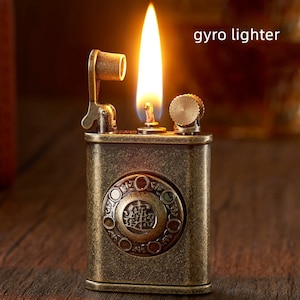 May include: A vintage-style, antique gold-toned lighter with a rotary dial design. The lighter is lit and has a flame coming from the top. The text "gyro lighter" is visible in the image.