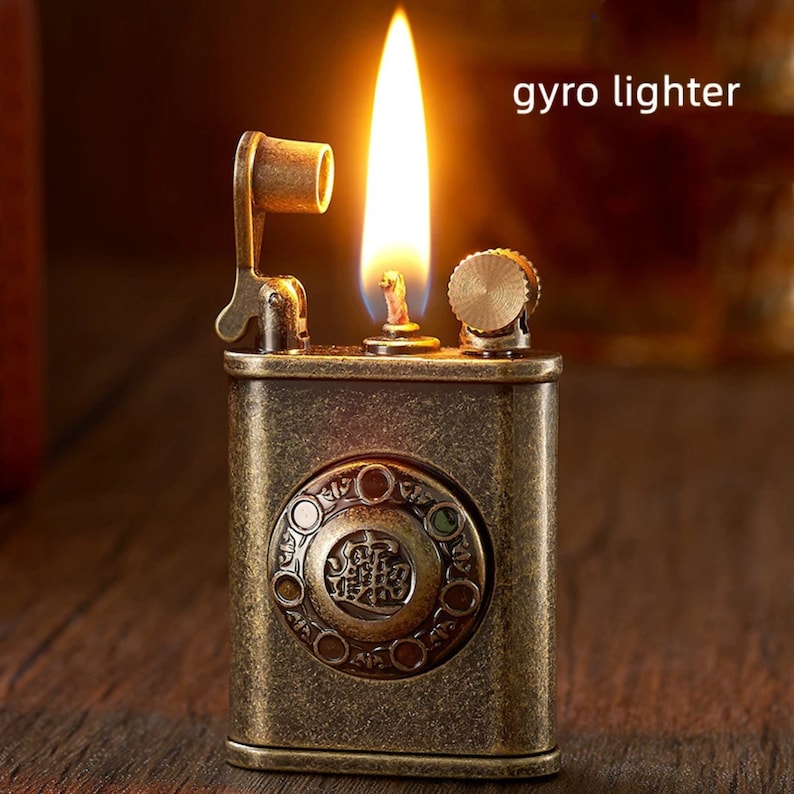 May include: A vintage-style, antique gold-toned lighter with a rotary dial design. The lighter is lit and has a flame coming from the top. The text "gyro lighter" is visible in the image.