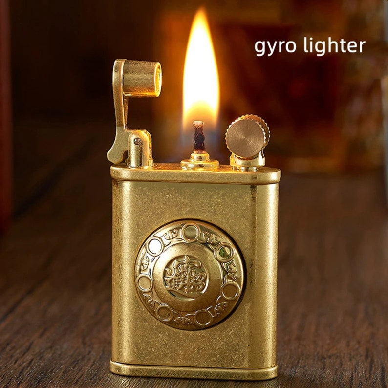 May include: A gold-toned metal lighter with a decorative design and a small flame. The lighter has a lever on the side and a small knob on the top. The text "gyro lighter" is visible in the image.