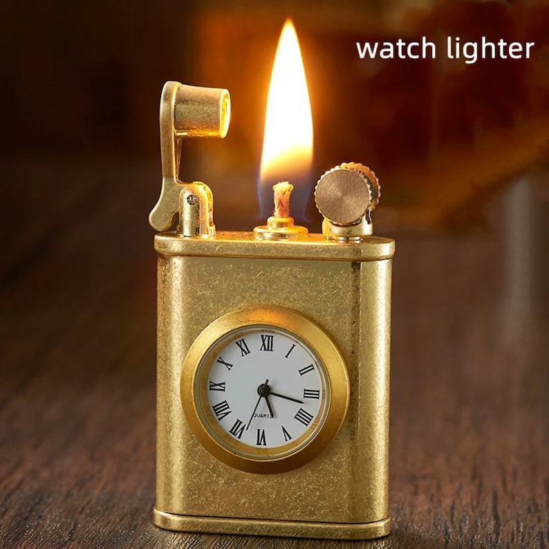 May include: A gold-toned watch lighter with a built-in clock face. The lighter has a flame coming out of the top and a small lever on the side.