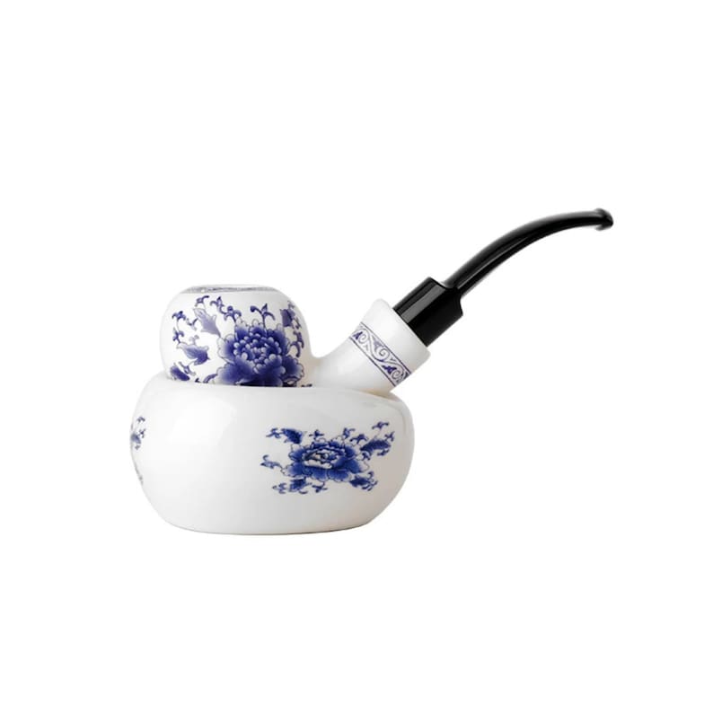 May include: A white ceramic pipe with a blue floral design. The pipe has a black stem and a bowl that is shaped like a flower.