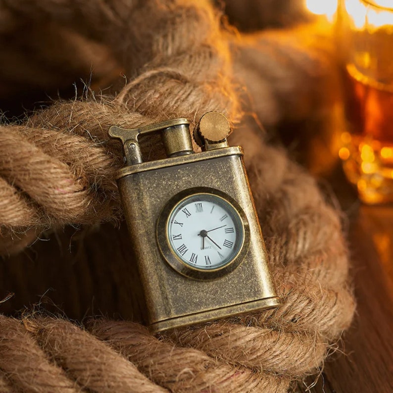 May include: A vintage-style lighter with a built-in clock face. The lighter is made of brass and has a dark brown patina. The clock face is white with black Roman numeral hour markers and black hands.