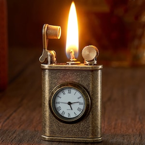 May include: A vintage-style lighter with a built-in clock face. The lighter is made of brass and has a textured finish. The clock face is white with black Roman numeral hour markers and black hands. The lighter is lit and the flame is visible.