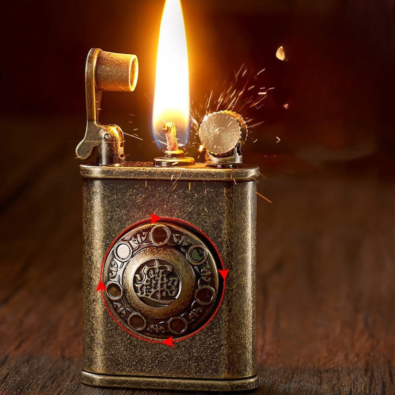 May include: A vintage-style lighter with a brass finish and intricate details. The lighter has a round, ornate design with a Chinese character in the center. The lighter is lit and has a flame coming out of the top.