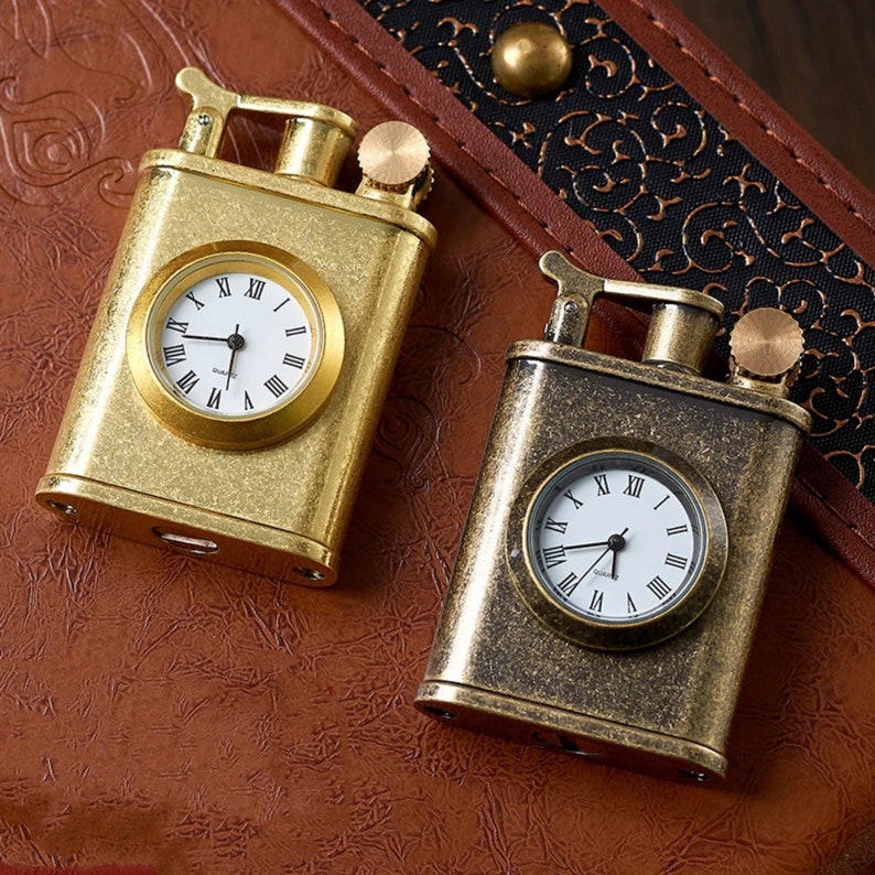May include: Two antique-style gold and brass lighters with built-in clocks. The lighters have a vintage design and are perfect for collectors.