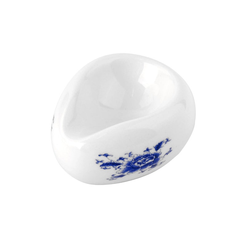 May include: A white ceramic teacup with a blue floral design. The cup is shaped like an egg and has a small lip.