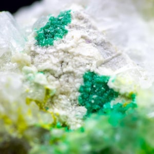 May include: Close-up of a mineral specimen with a crystalline structure. The image showcases a mix of colors, including white, green, and yellow. The green appears in clusters, while the yellow and white blend together.