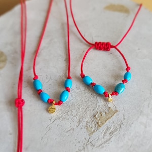 Peut inclure: Un collier en cordon rouge et un bracelet en cordon rouge assorti, tous deux ornés de perles ovales bleu vif et d'une petite breloque dorée texturée et ronde. Le bracelet possède un fermoir coulissant réglable, tandis que le collier est simple.
