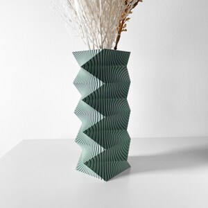 May include: A geometric green vase with a wavy pattern. The vase is made of paper and has a modern design.