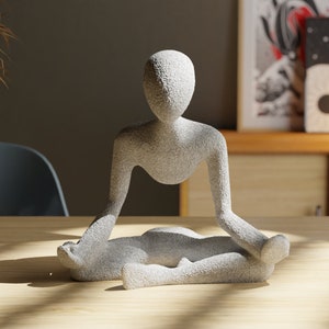 May include: A grey stone sculpture of a person sitting in a meditative pose with legs crossed and hands resting on their lap.