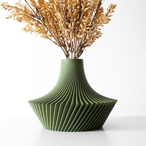 Könnte beinhalten: Eine grüne Keramikvase mit einem einzigartigen, gefalteten Design. Die Vase ist mit getrockneten, hellbraunen Blumen gefüllt.