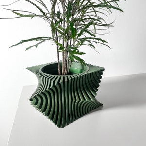 This planter pot exhibits a dynamic and architectural design, characterized by its series of vertical green pleats that create a striking corrugated effect reminiscent of modern art sculptures. The pleats produce a rhythmic pattern.