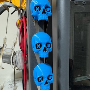 May include: Three vibrant blue skull ornaments, each featuring black cross and heart-shaped eye details. The skulls are arranged vertically, highlighting their distinctive decorative appeal. These ornaments bring a bold, alternative aesthetic to any setting.