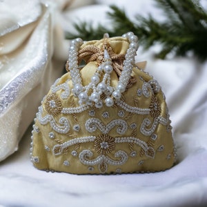 Peut inclure: Un sac à cordon doré avec un ornement de perles et de perles dorées. Le sac est décoré d'un motif floral.