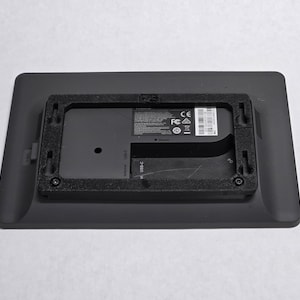 May include: The back of a black digital picture frame with a black plastic frame around the screen. The frame has a label with the text "FCC ID: 2A38T-FPD", "CE", and "Microsoft" printed on it.