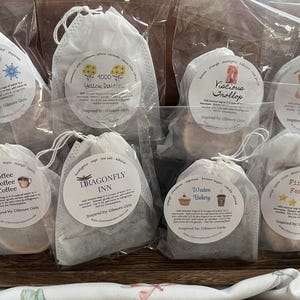 May include: Eight small white muslin bags containing different tea blends. The bags are labelled with names such as "I Smell Snow", "1000 Yellow Daisies", "Coffee Coffee Coffee", "Dragonfly Inn", "Viscious Trollop", "Copper Boom", "Weston Bakery", and "Firelight Festival".