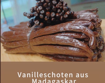 Könnte beinhalten: Nahaufnahme eines Bündels dunkelbrauner Vanilleschoten aus Madagaskar. Die Schoten sind in einem ordentlichen Stapel angeordnet, wobei die Enden der Schoten sichtbar sind. Der Text "Frische Ernte 2024" und "Vanilleschoten aus Madagaskar" ist oben und unten im Bild sichtbar.
