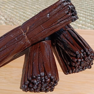 Könnte beinhalten: Drei Bündel getrockneter Vanilleschoten, mit Schnur zusammengebunden, auf einer Holzoberfläche. Die Schoten sind dunkelbraun und haben einen reichen, aromatischen Duft.