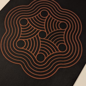 May include: An abstract geometric design in black and copper with a circular pattern. The design is made up of concentric circles and wavy lines.