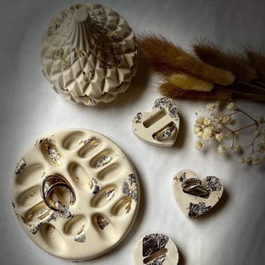 Könnte beinhalten: Ein Set aus vier weißen Keramik-Ringtellern mit Blattgold-Akzenten. Die Teller sind in Form einer Kuppel, eines Herzens, eines Kreises und eines Tabletts mit mehreren Fächern gestaltet.