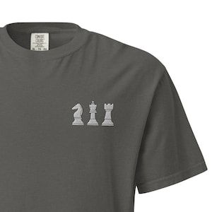 Könnte beinhalten: Ein dunkelgraues T-Shirt mit einem weißen gestickten Design aus vier Schachfiguren: einem Springer, einem Bauern, einem Turm und einem König.