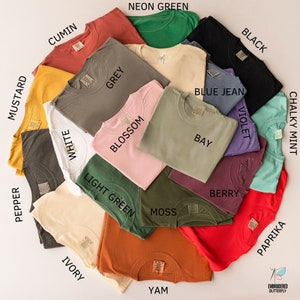 May include: A flat lay of 16 different colored t-shirts, each with a different color name written on the fabric. The colors include mustard, pepper, cumin, white, ivory, grey, blossom, light green, neon green, moss, blue jean, bay, berry, violet, black, paprika, and yam.