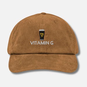 Könnte beinhalten: Eine braune Baseballkappe aus Cord mit einem weißen gestickten Design eines Bierglases und dem Text "VITAMIN G".