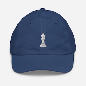 Puede incluir: Gorra de béisbol azul marino con una reina de ajedrez bordada en blanco. La gorra tiene una visera curva y un diseño de seis paneles, con un botón en la parte superior.