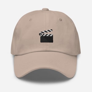 May include: A beige baseball cap with an embroidered black and white clapperboard design.