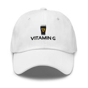 May include: White baseball cap featuring a black and yellow pint of stout graphic and the text "VITAMIN G". The cap has a curved peak and an adjustable strap. A stylish accessory for casual wear.