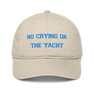 May include: A beige baseball cap with the text "NO CRYING ON THE YACHT" embroidered in blue.