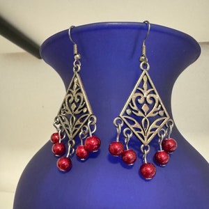 May include: A pair of silver dangle earrings with a diamond-shaped filigree design and red bead accents.