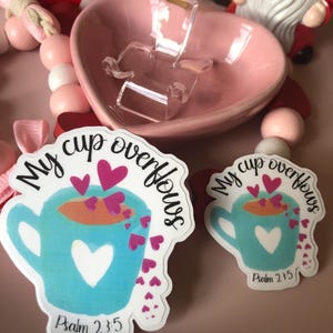 May include: Two white stickers with a blue cup overflowing with pink hearts. The text on the stickers reads "My cup overflows" and "Psalm 23:5".