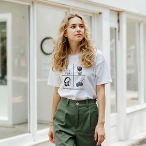 May include: A white short-sleeved t-shirt featuring a black graphic print divided into four quadrants containing a dog, a bubble tea, headphones, and yarn with needles, with the text "The only algorithm that matters" printed below.