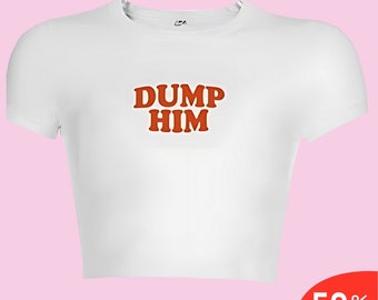 Puede incluir: Top corto blanco con el texto "DUMP HIM" en letras naranjas. La camiseta tiene mangas cortas y cuello redondo. Un banner rojo en la esquina inferior derecha muestra "50% OFF".