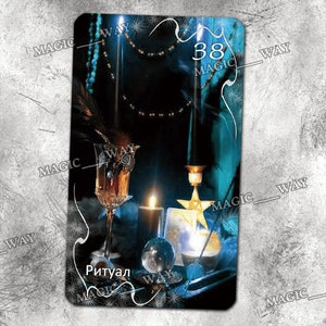 May include: A dark blue tarot card with the number 38 and the word "MAGIC" printed on it. The card features a still life of a lit candle, a crystal ball, a glass of liquid, and a feather. The word "RITUAL" is printed in white at the bottom of the card.